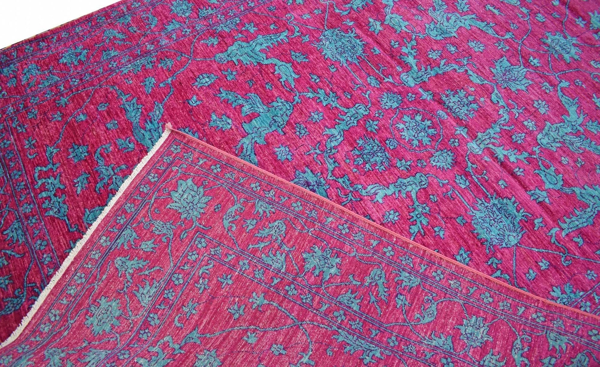 An Afghan Chobi rug featuring a vibrant magenta background with intricate teal floral patterns.