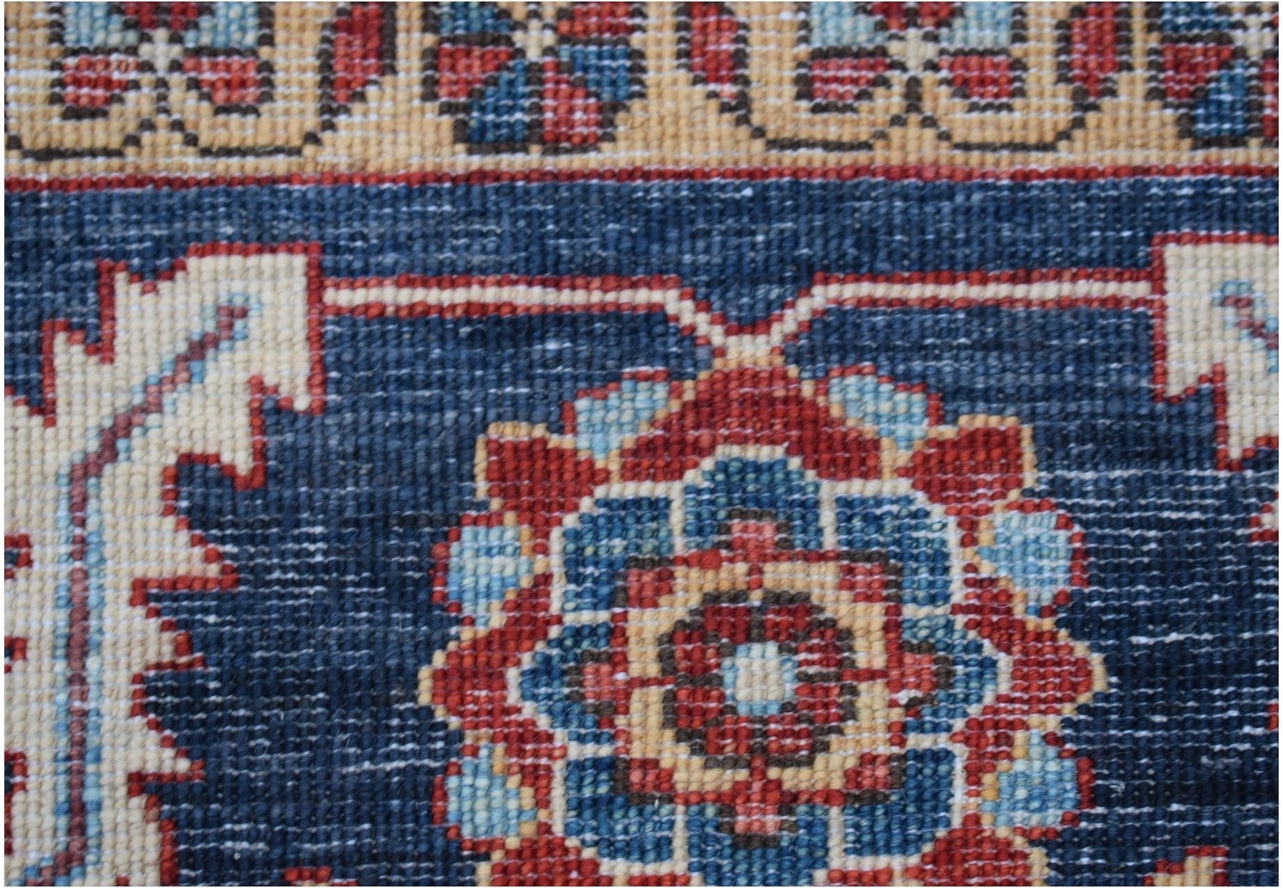 A close-up of a handmade Afghan Chobi rug featuring a floral medallion on a deep blue field.