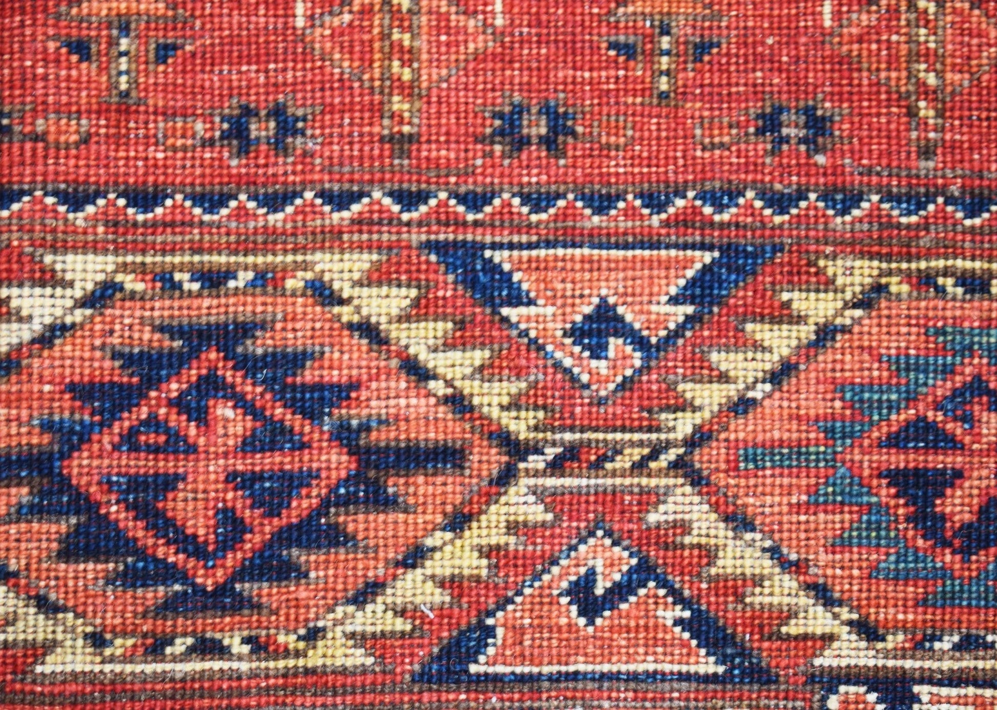 A close-up of a handwoven Afghan Chobi rug featuring traditional geometric patterns in red and blue.