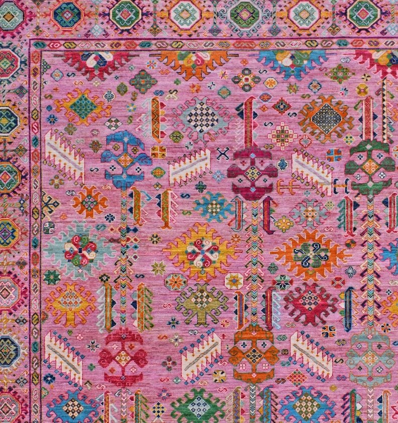 A handwoven Afghan Chobi rug featuring a vibrant pink field with colorful geometric motifs.