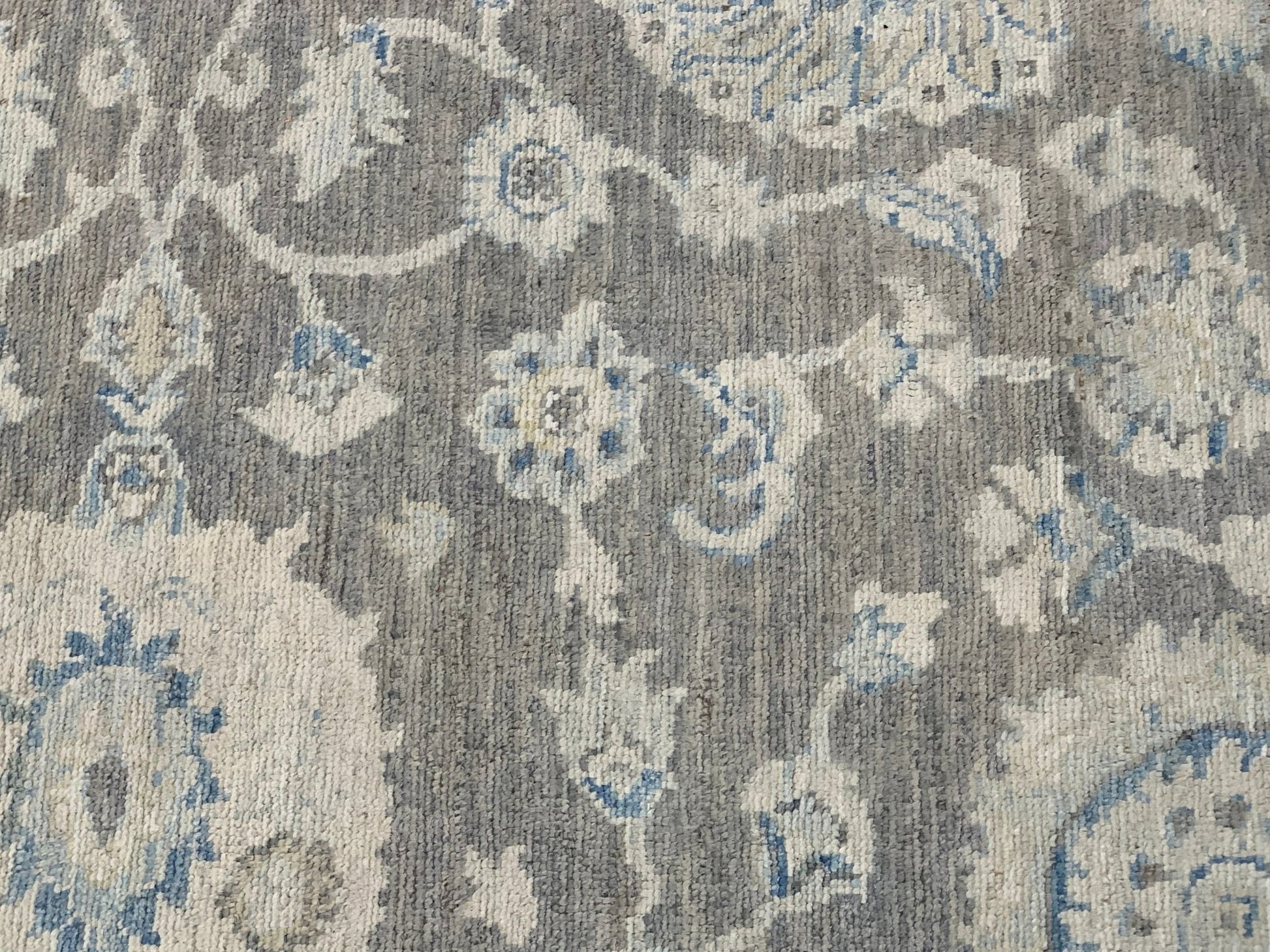 A handmade Afghan Chobi rug featuring a traditional floral pattern in shades of grey and blue.