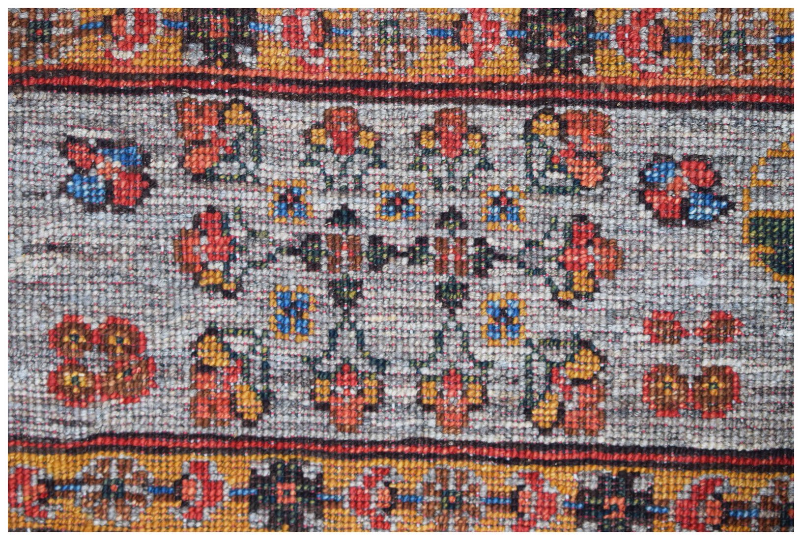 A close-up of an Afghan Chobi rug featuring a central floral motif in warm tones on a grey field.