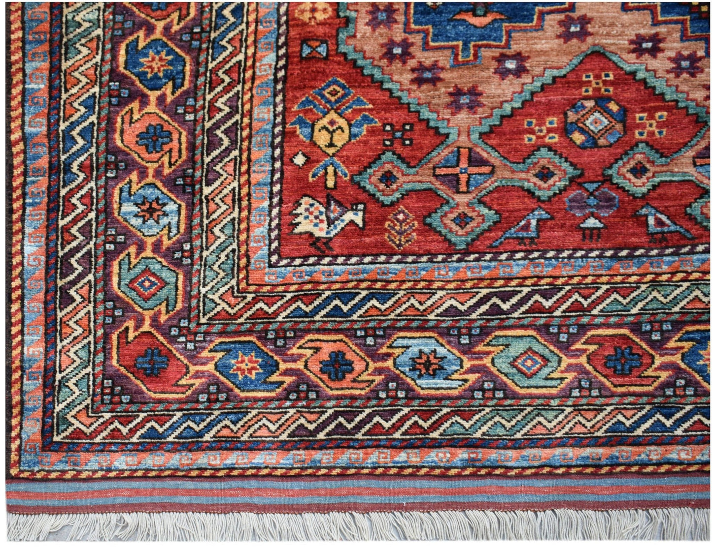 A handmade Afghan Herati rug featuring intricate geometric patterns in red, blue, and orange tones.