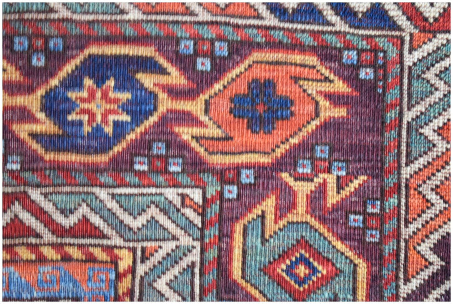 A close-up of an Afghan Herati rug featuring intricate geometric patterns in blue, orange, and red.