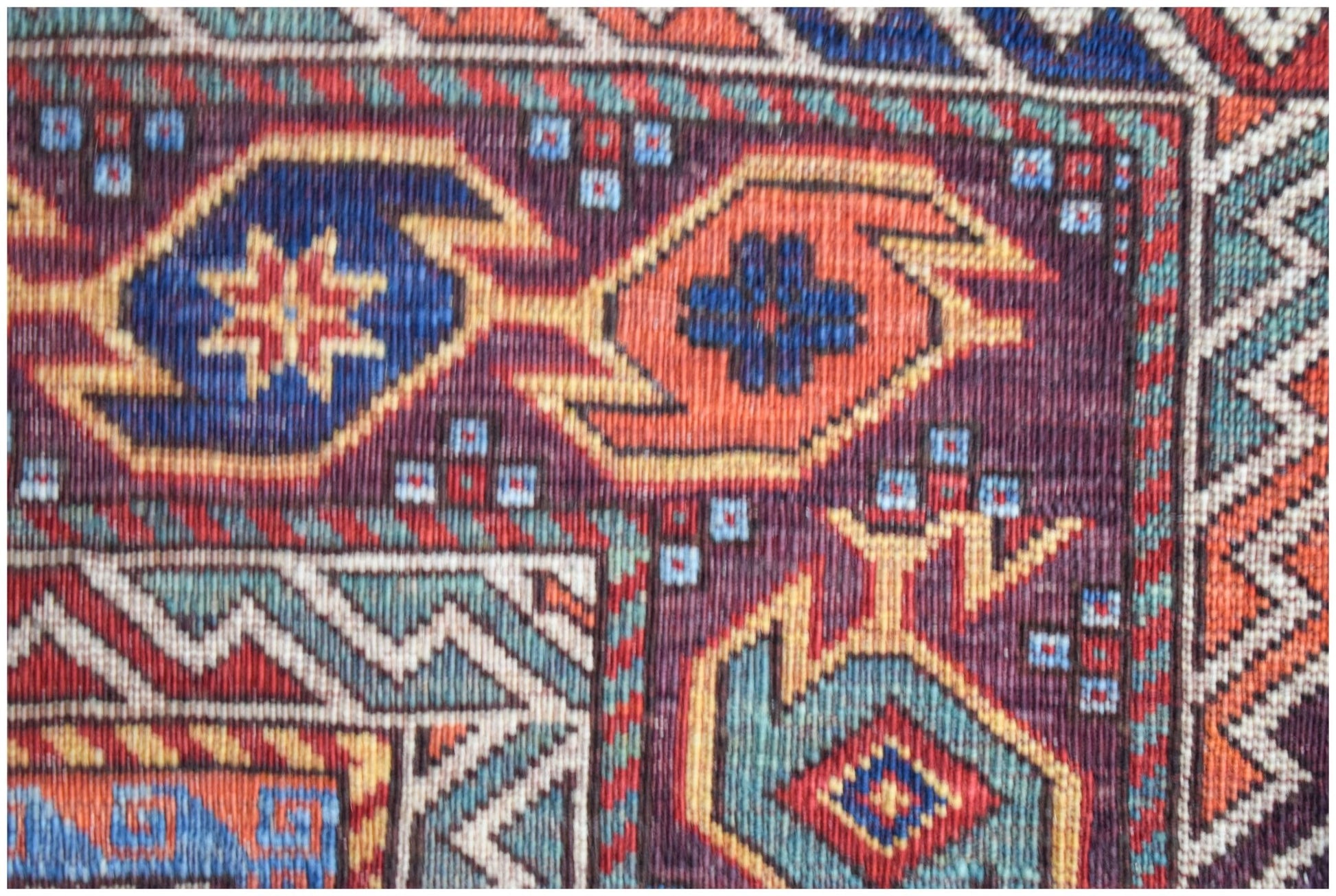 A close-up of an Afghan Herati rug featuring intricate geometric patterns in blue, orange, and red.