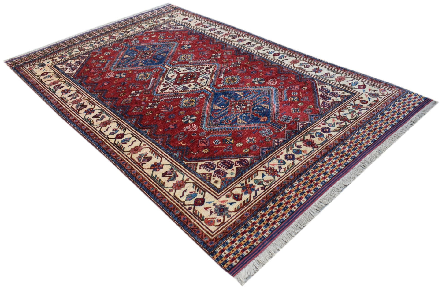 An Afghan Herati rug featuring a traditional red field with blue geometric medallions and fringe.