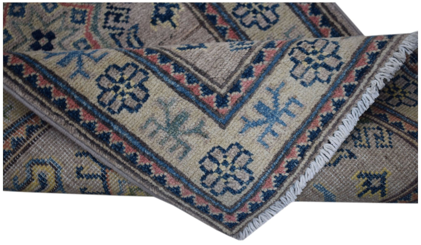 A folded Afghan Kazakh runner rug featuring traditional geometric motifs in blue, pink, and tan.