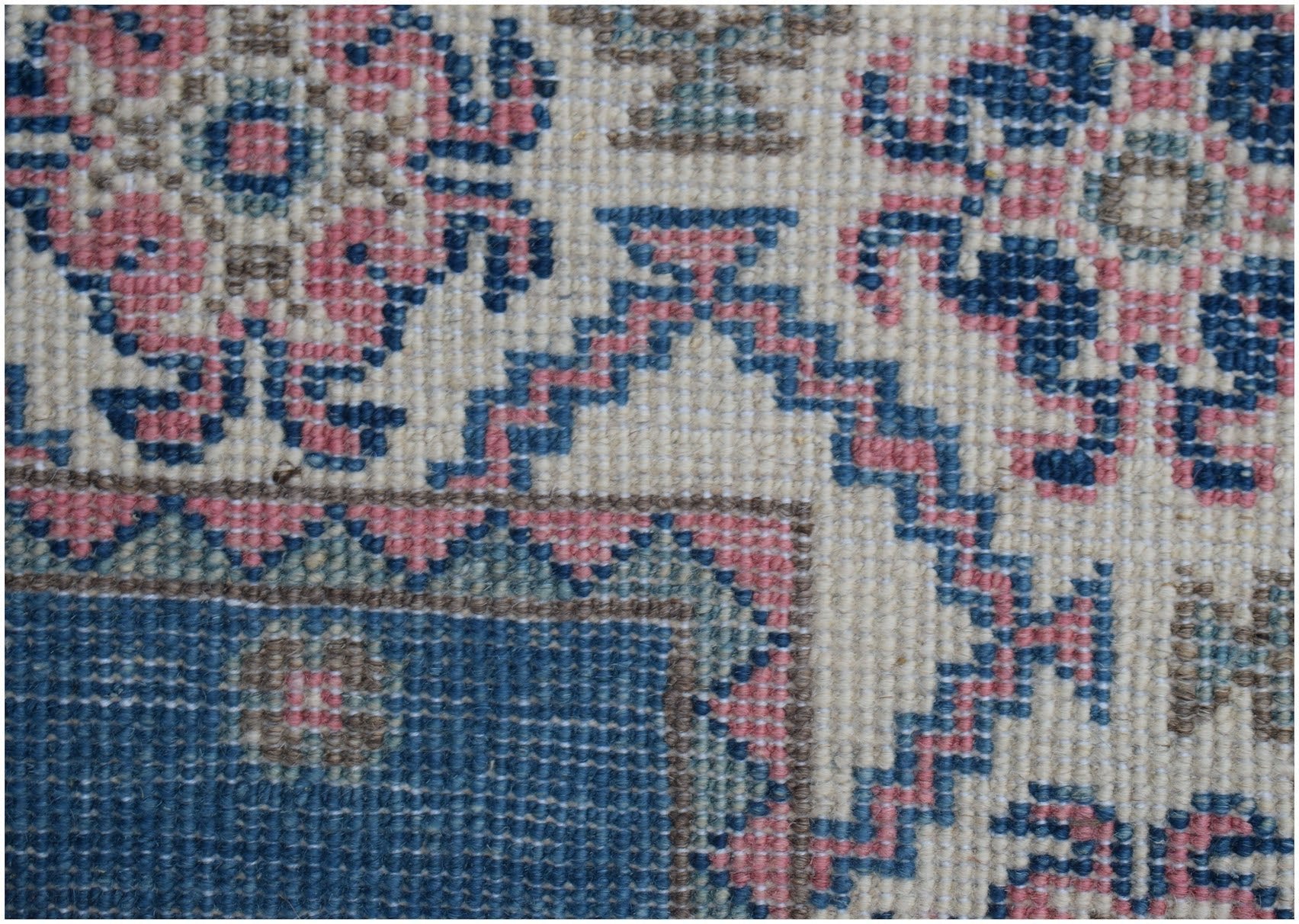 A close-up of an Afghan Kazakh runner featuring traditional geometric motifs in blue and pink wool.