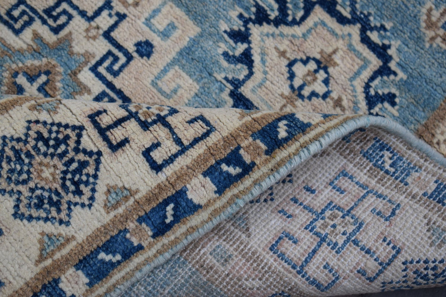 A handmade Afghan Kazakh runner rug featuring a geometric pattern in shades of blue and beige.