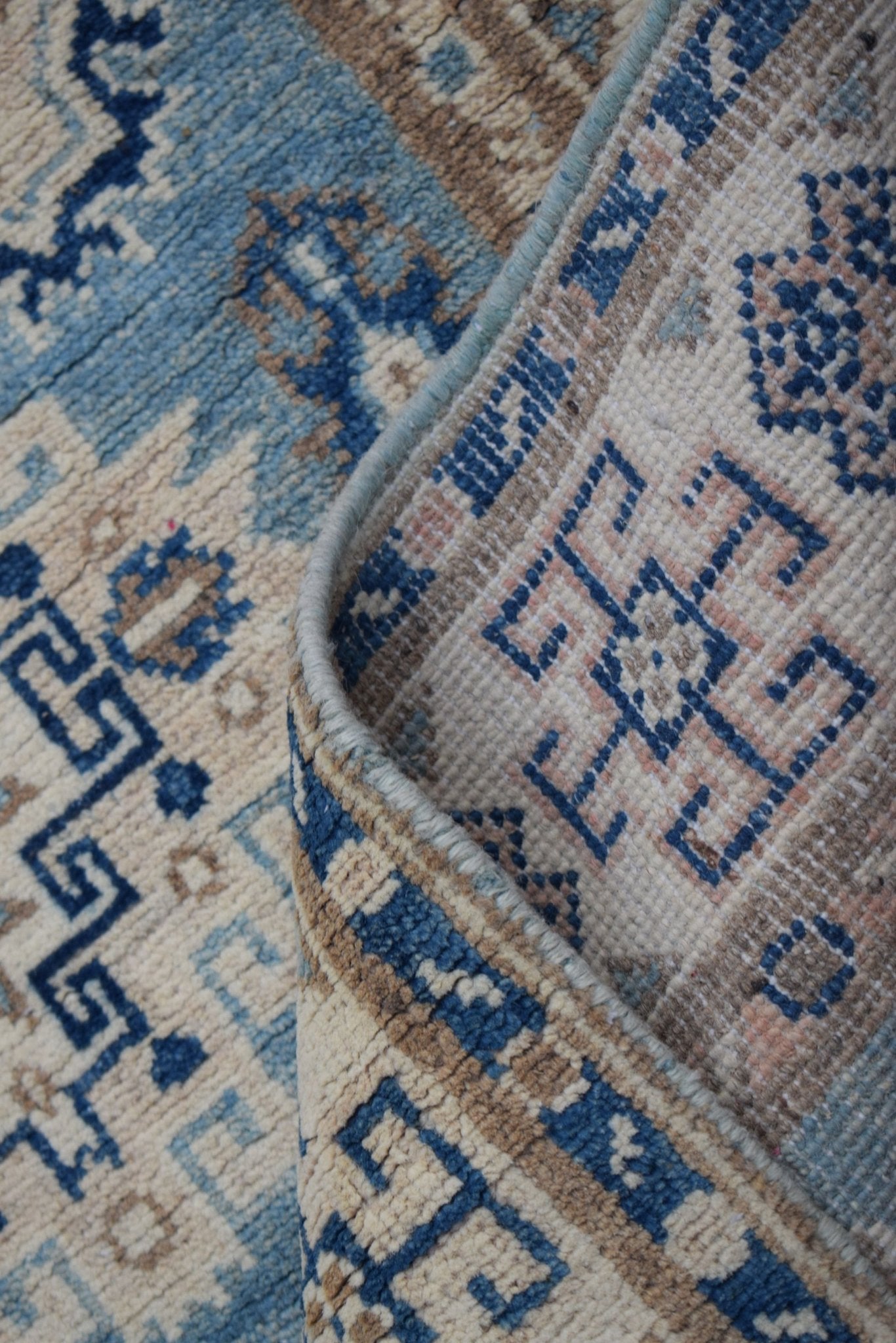 A handmade Afghan Kazakh runner featuring a geometric pattern in shades of blue, beige, and grey.