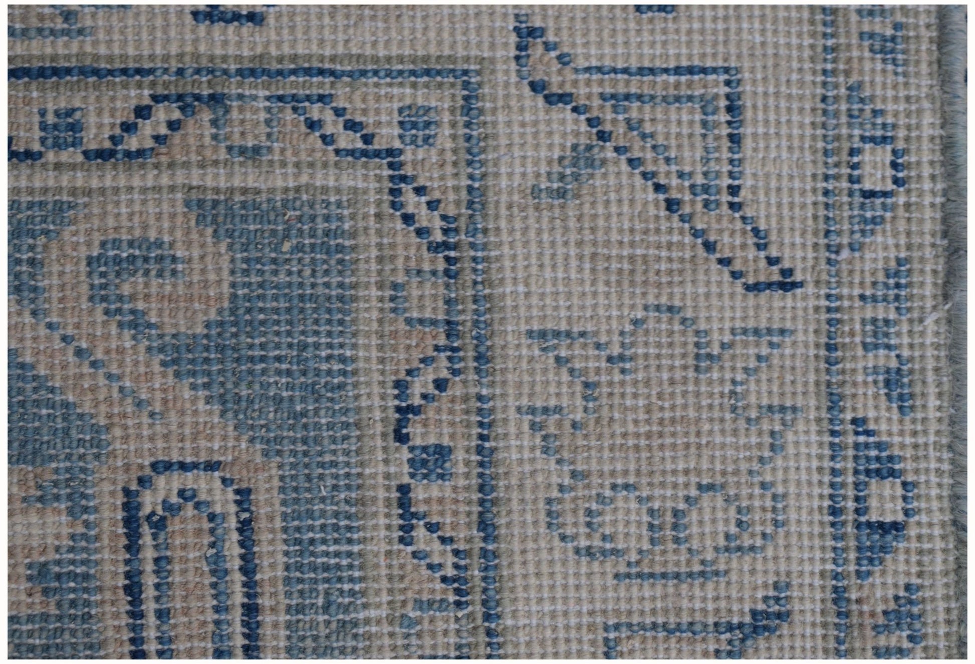 A close-up view of an Afghan Kazakh runner rug featuring blue geometric patterns on a beige base.