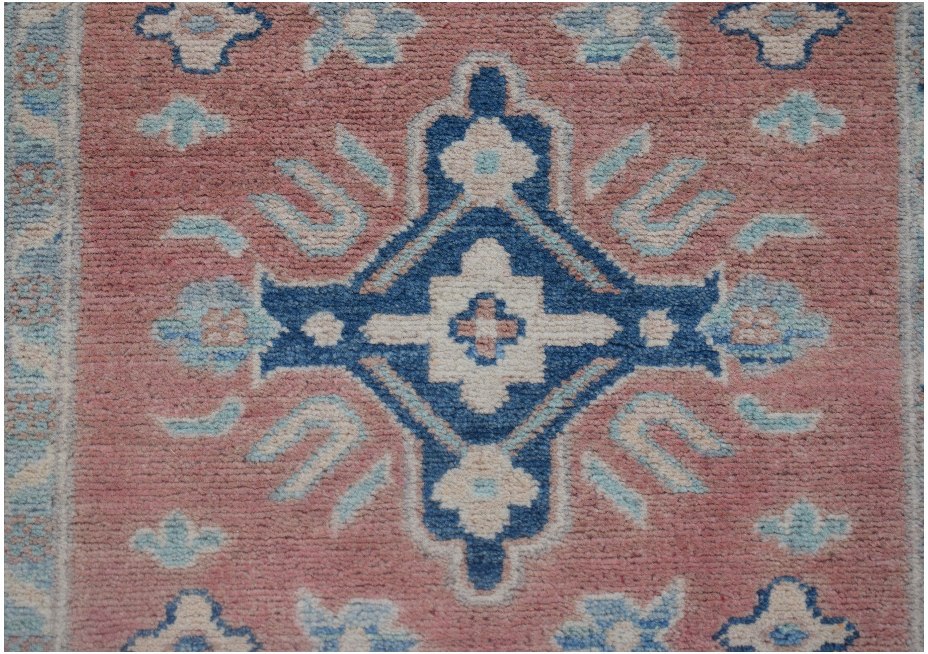 A handmade Afghan Kazakh runner featuring a central blue geometric medallion on a dusty pink field.