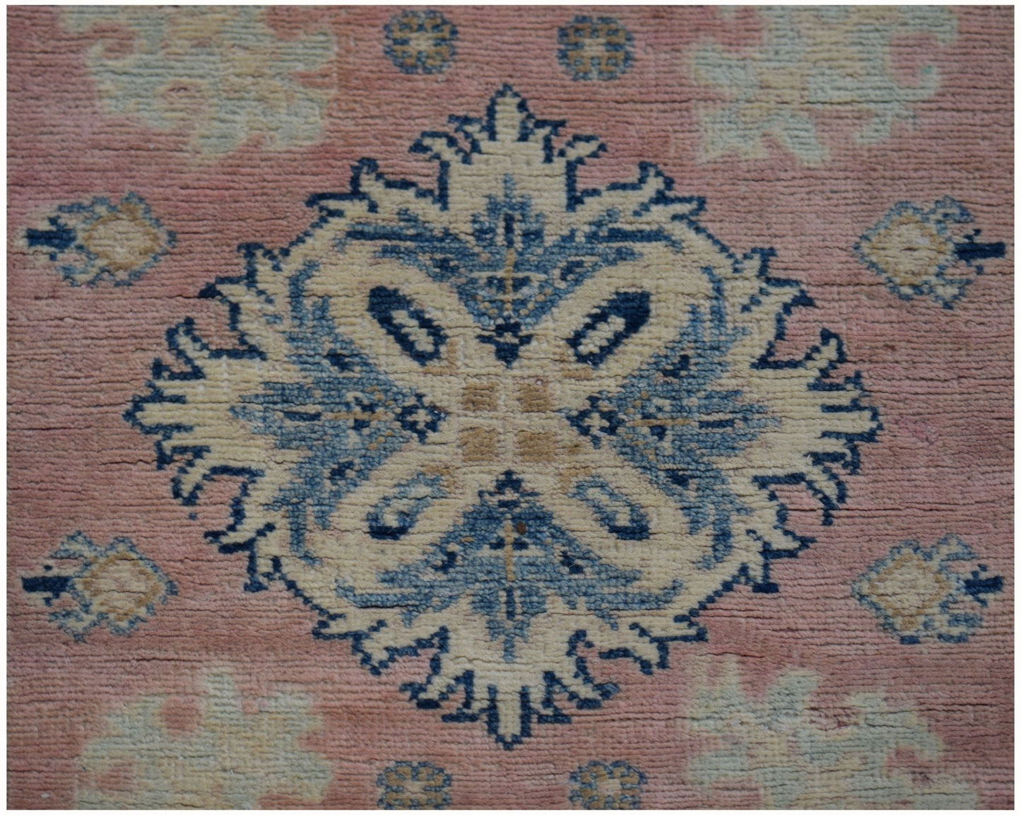 A handmade Afghan Kazakh runner featuring a central blue and beige floral medallion on a pink field.