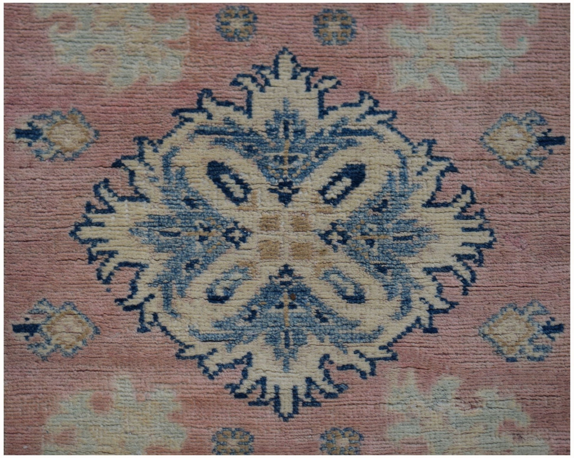 A handmade Afghan Kazakh runner featuring a central blue and beige floral medallion on a pink field.