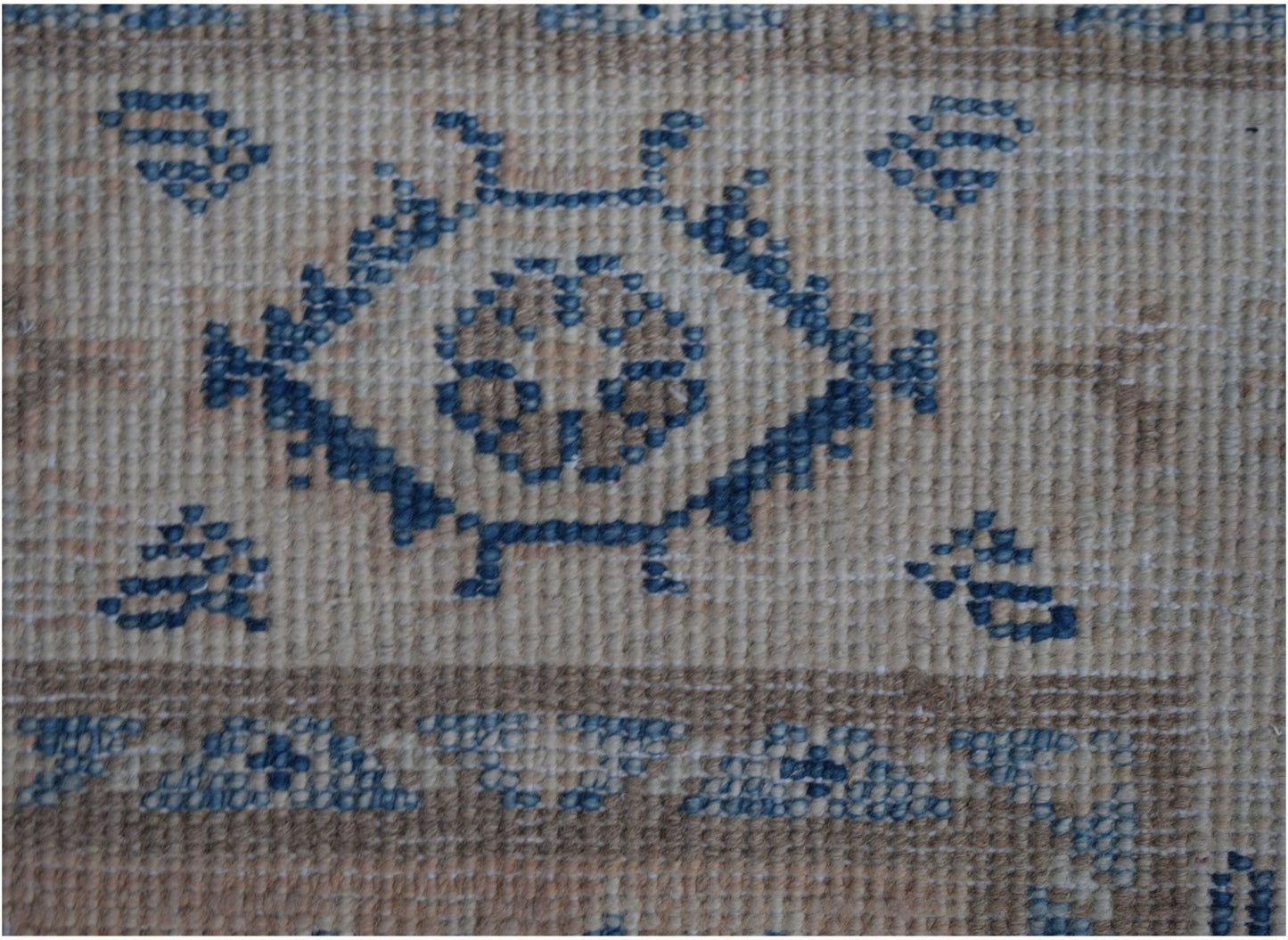 A close-up of an Afghan Kazakh runner rug featuring a blue geometric floral motif on a beige base.