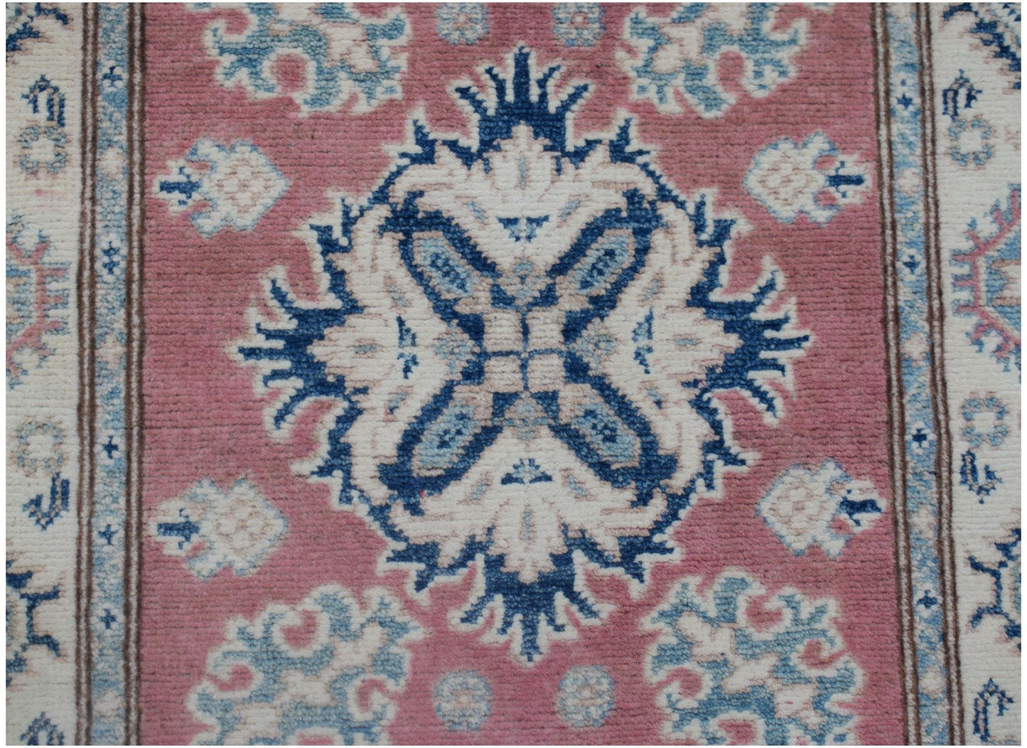 An Afghan Kazakh runner featuring a central blue and white floral medallion on a pink background.