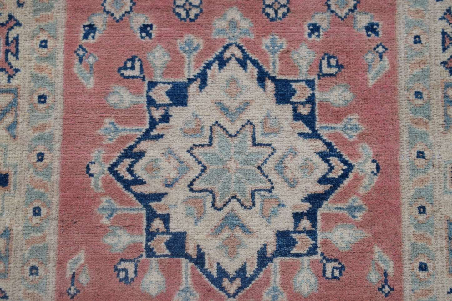 Handmade Afghan Kazakh runner featuring a central blue and cream star medallion on a pink field.