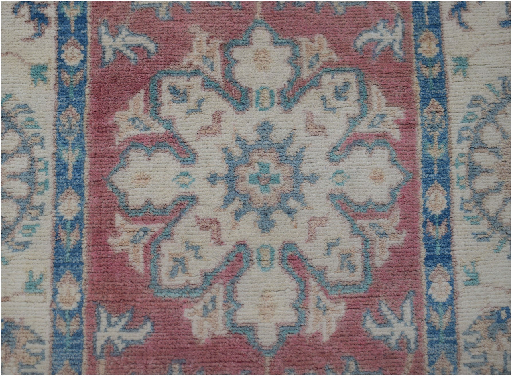 Handmade Afghan Kazakh runner featuring a central floral medallion in pink, blue, and cream wool.