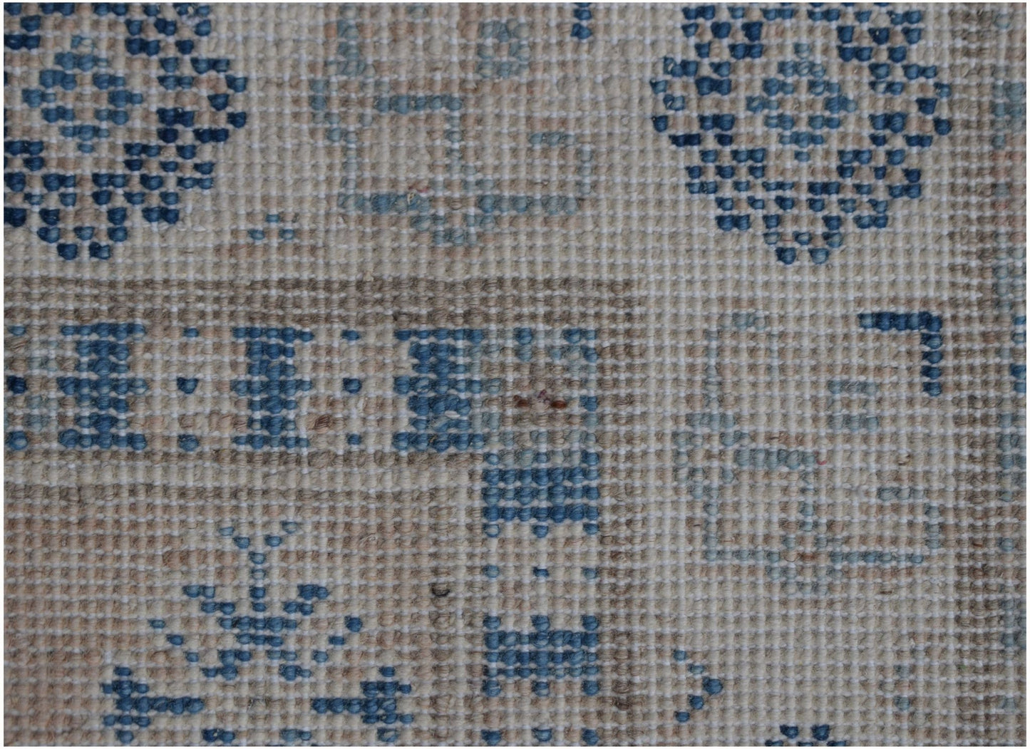 A close-up of a handmade Afghan Kazakh runner featuring geometric blue patterns on a tan wool base.