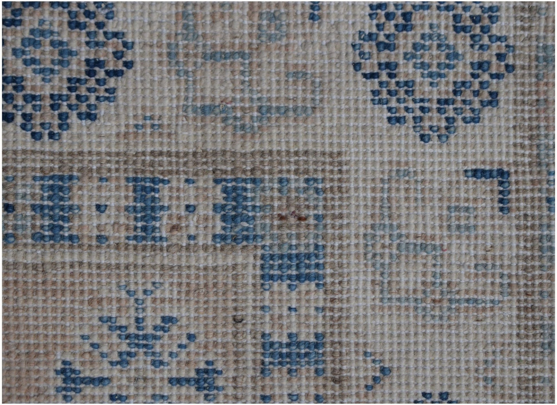 A close-up of a handmade Afghan Kazakh runner featuring geometric blue patterns on a tan wool base.