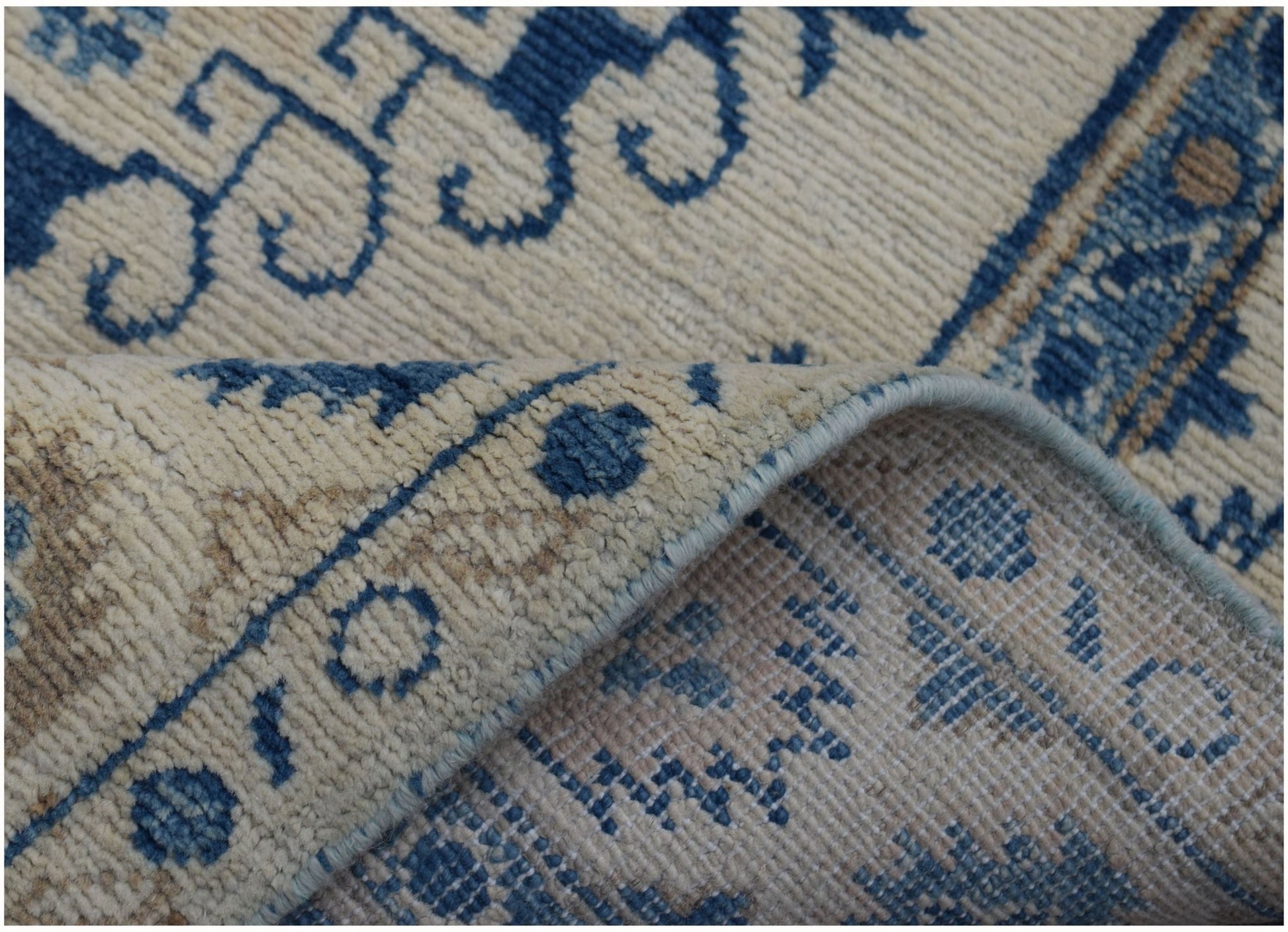 A corner of a handmade Afghan Kazakh runner featuring blue traditional patterns on a cream background.
