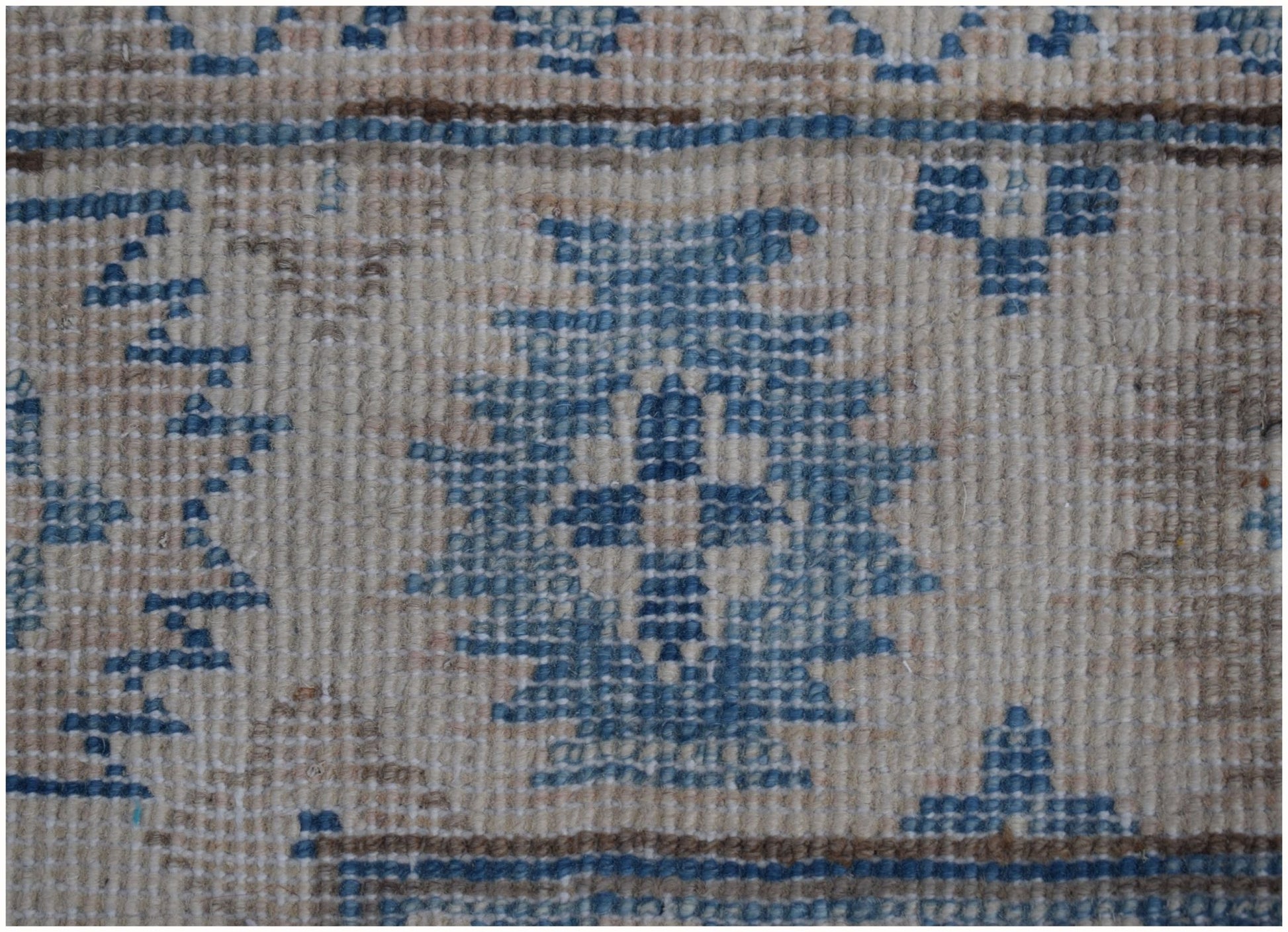 A close-up of a handmade Afghan Kazakh runner featuring blue geometric motifs on a beige wool field.