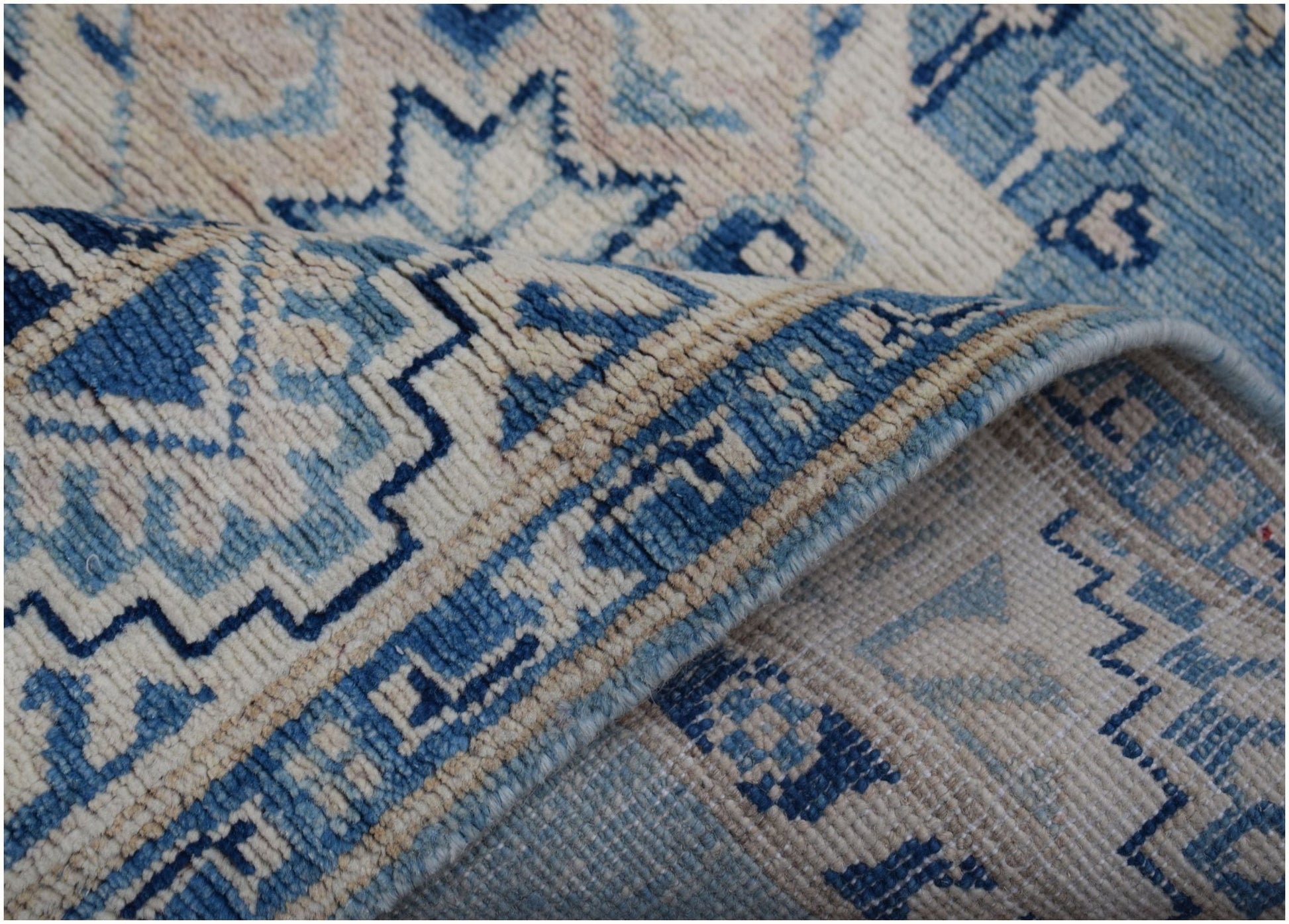 A handmade Afghan Kazakh runner rug featuring a geometric pattern in shades of blue and beige.