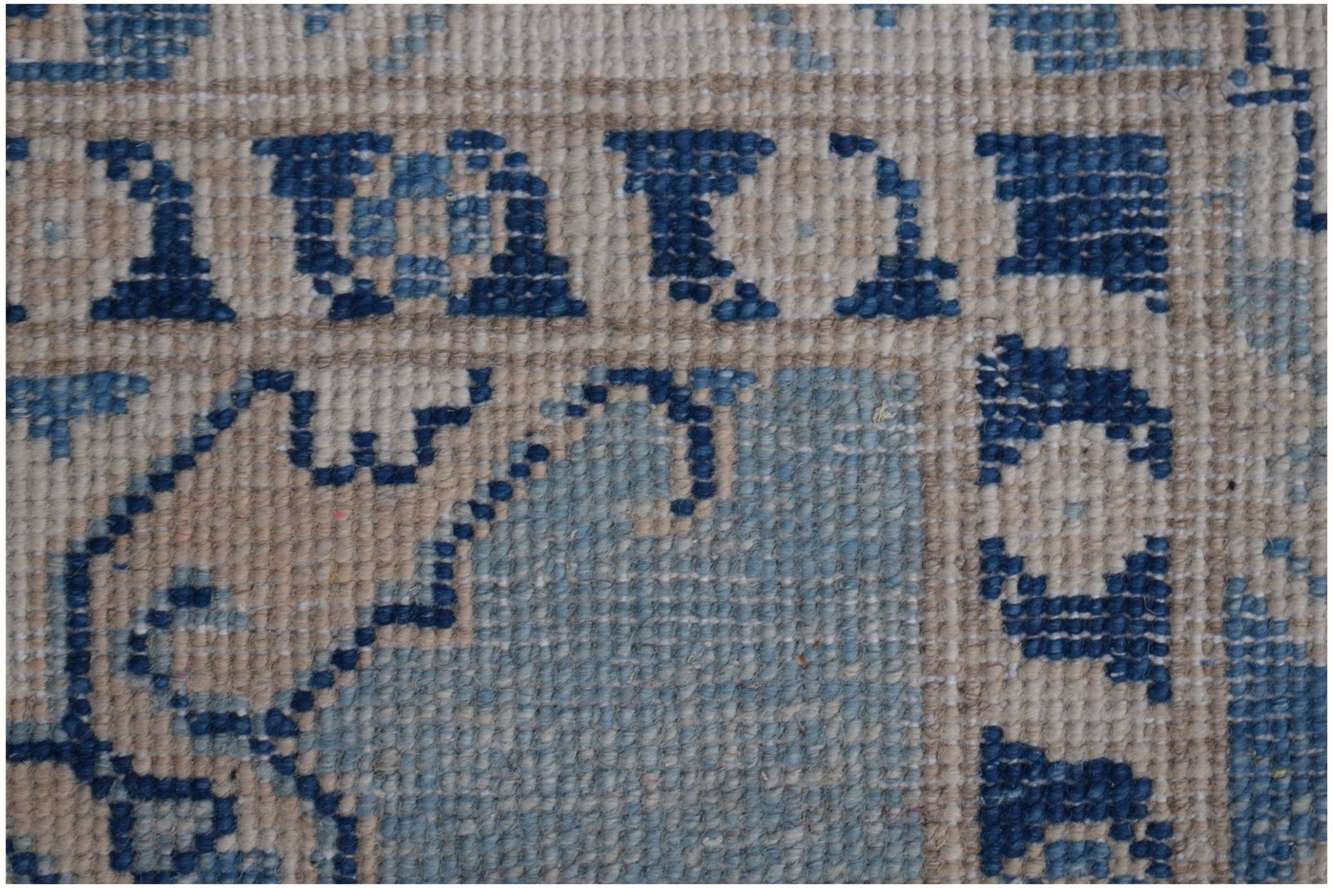 A close-up of a handmade Afghan Kazakh runner featuring a geometric blue and beige wool pattern.