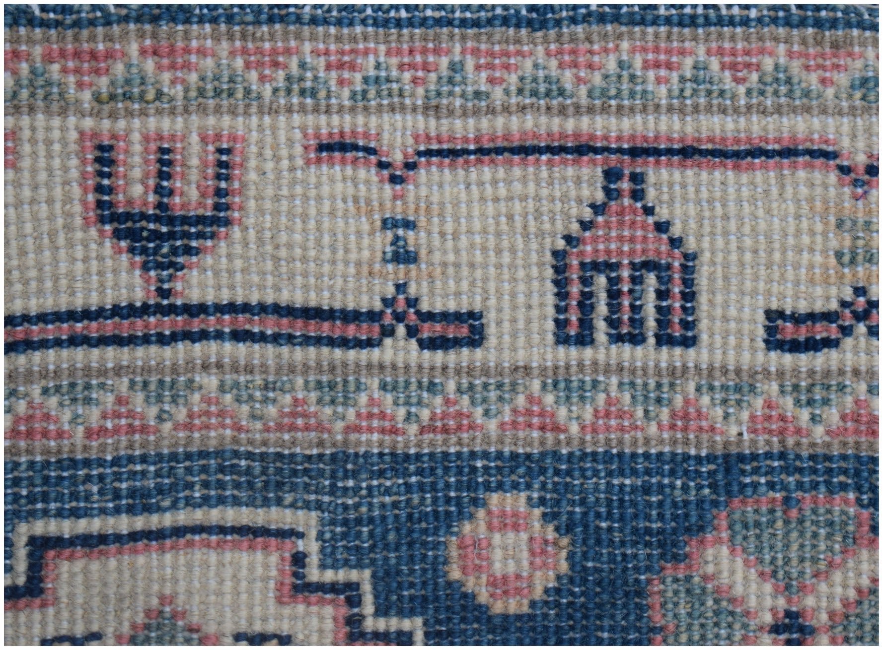 A close-up of an Afghan Kazakh runner featuring traditional geometric motifs in blue and pink wool.