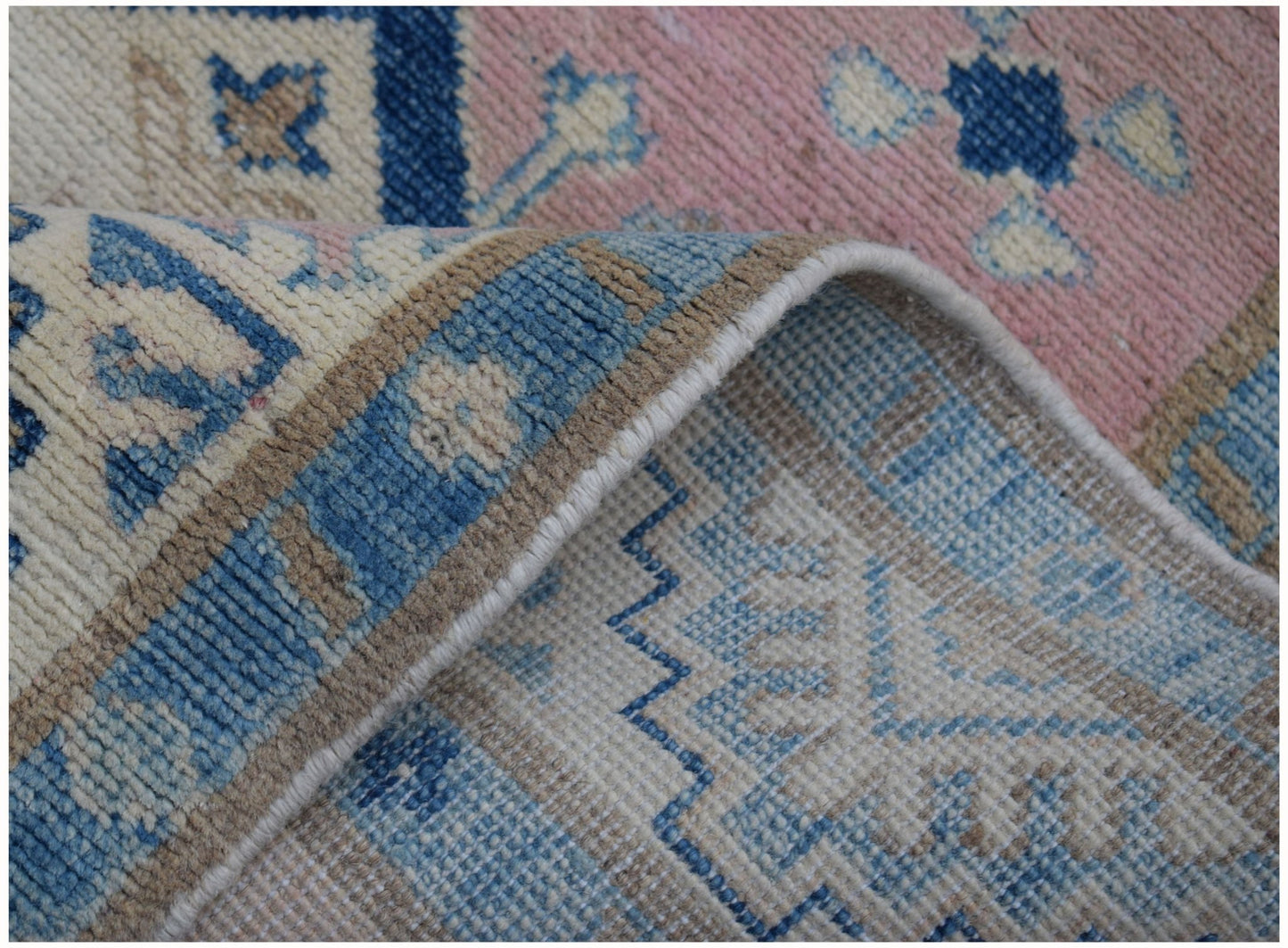A close-up of a handmade Afghan Kazakh runner featuring a geometric pattern in blue, pink, and beige.
