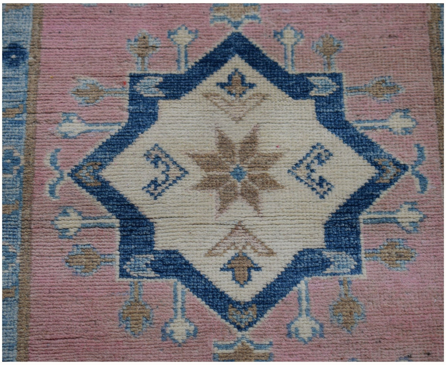 An Afghan Kazakh runner rug featuring a central blue and beige star medallion on a pink field.