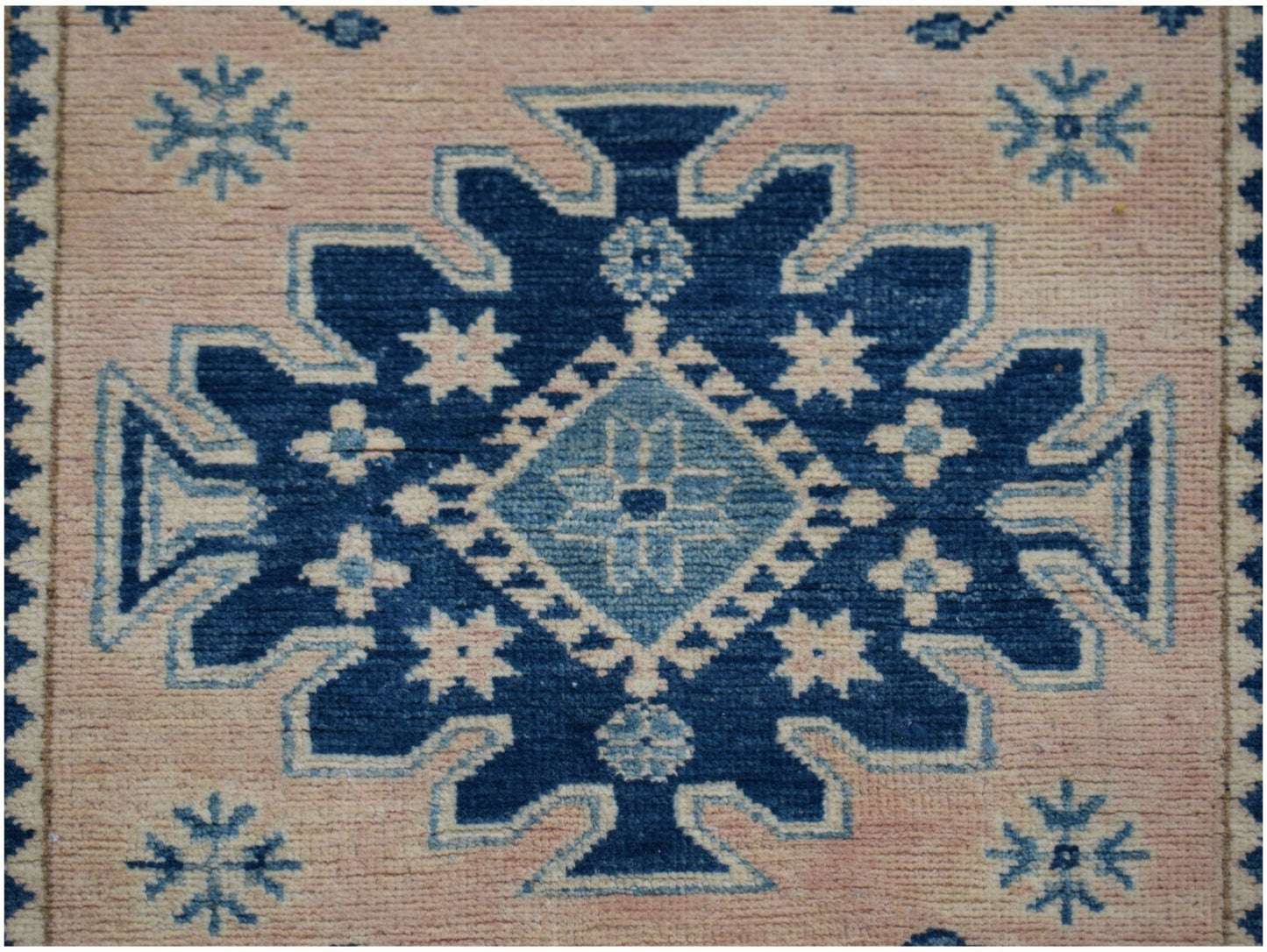 A handmade Afghan Kazakh runner rug featuring a central blue geometric medallion on a beige field.