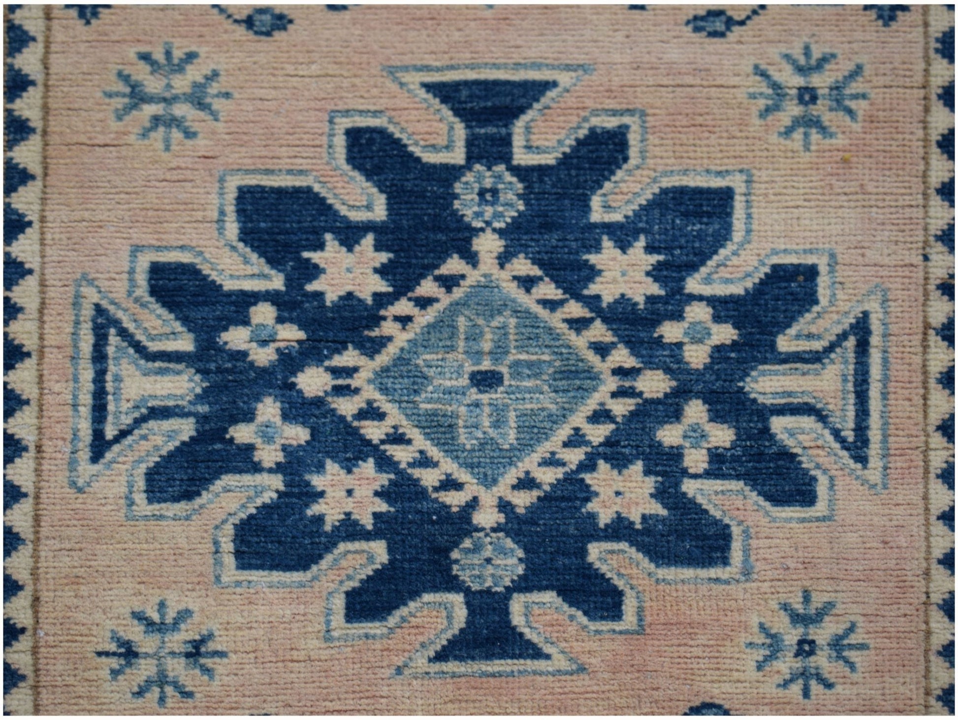 A handmade Afghan Kazakh runner rug featuring a central blue geometric medallion on a beige field.