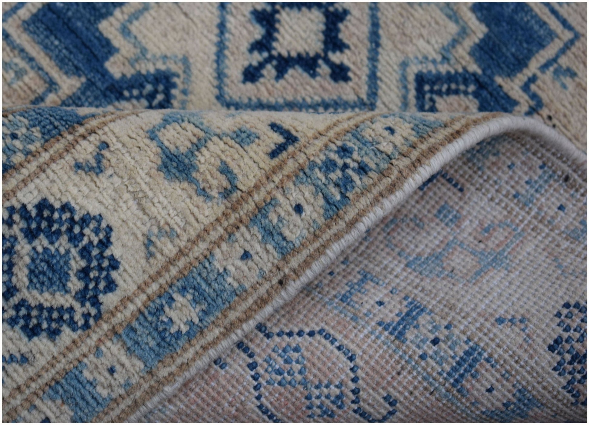 A handmade Afghan Kazakh runner featuring a blue and beige geometric pattern on a wool pile.