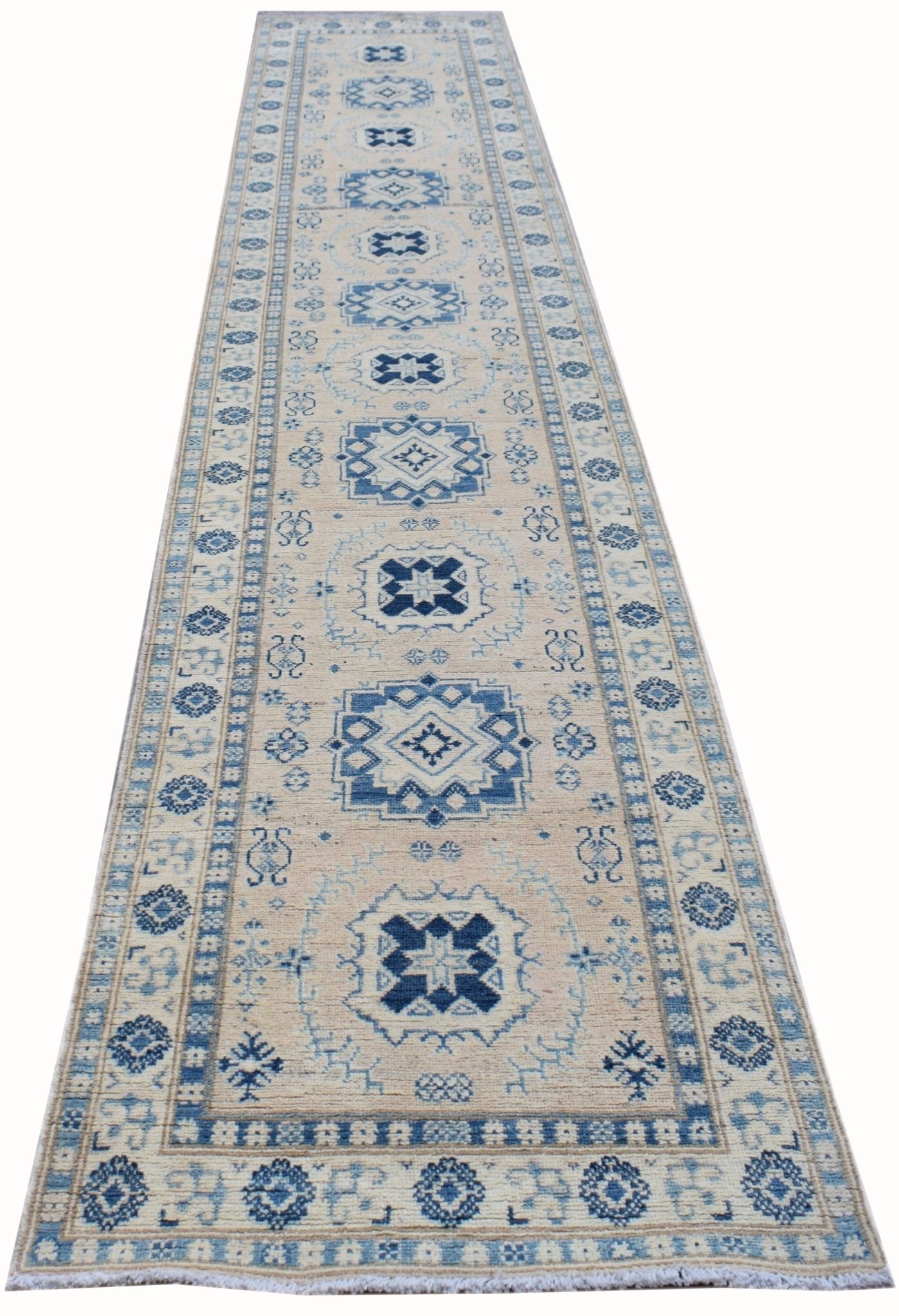 A handmade Afghan Kazakh runner rug featuring a geometric blue pattern on a beige wool background.