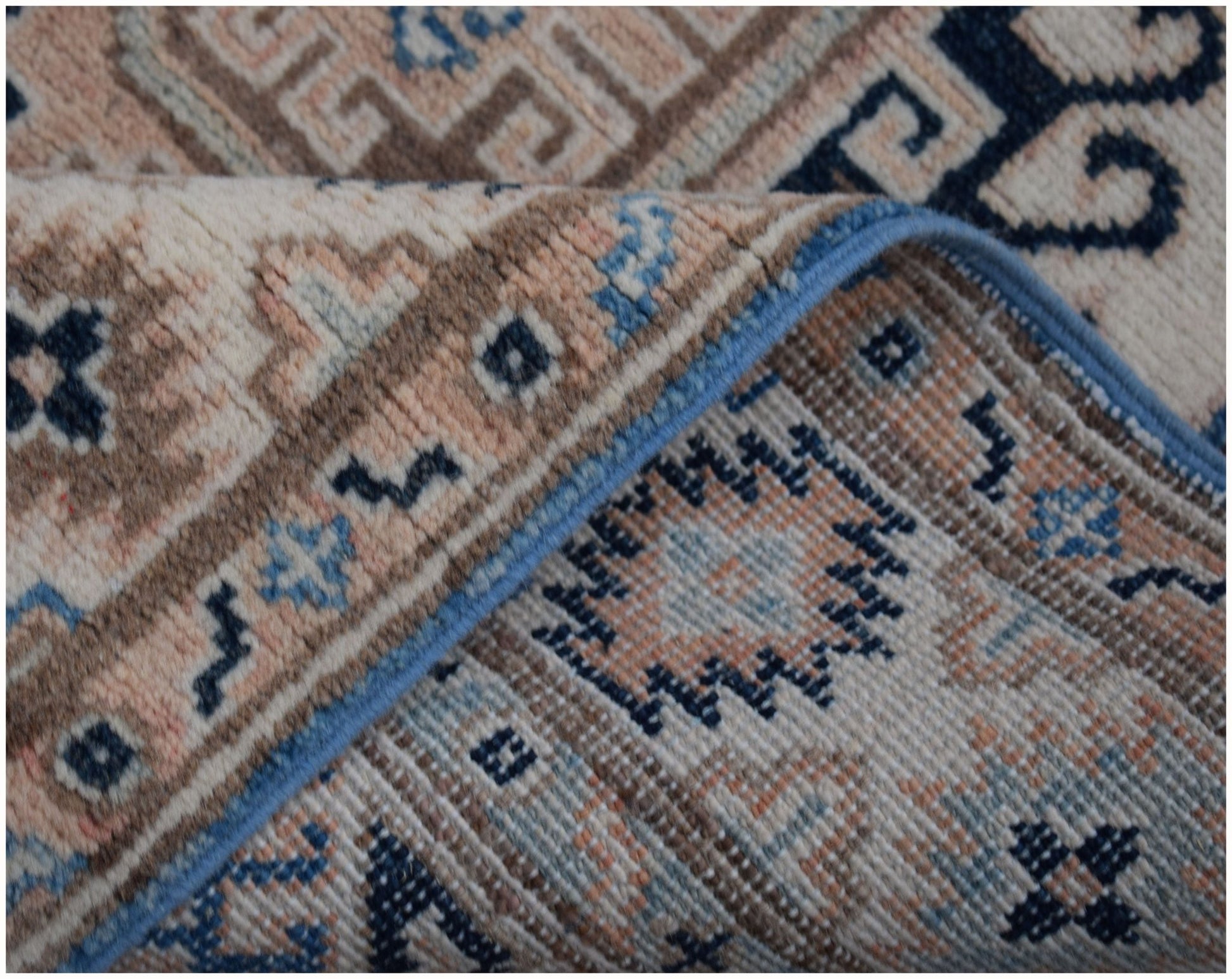 A folded Afghan Kazakh runner rug featuring a geometric pattern in shades of beige and blue.