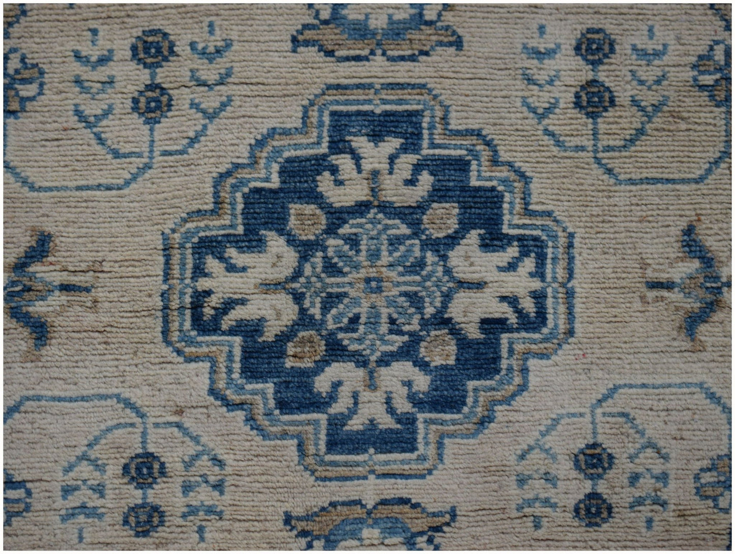 Handmade Afghan Kazakh runner featuring a central blue geometric medallion on a beige wool field.