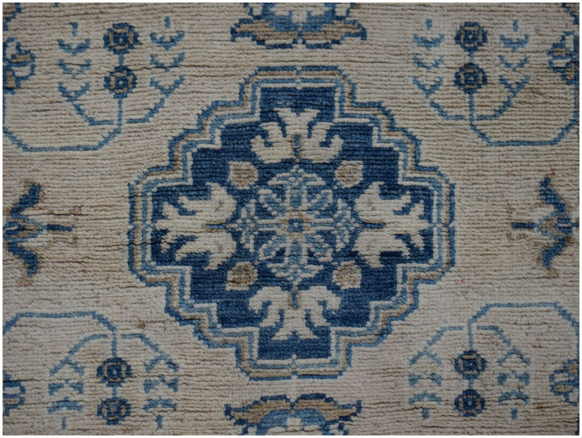 Handmade Afghan Kazakh runner featuring a central blue geometric medallion on a beige wool field.
