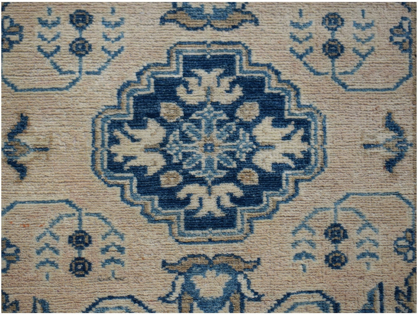 An Afghan Kazakh runner rug featuring a central blue geometric medallion on a beige wool field.