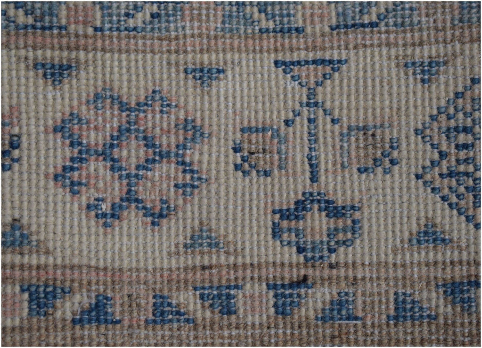 A close-up of a handmade Afghan Kazakh runner featuring a beige wool pile with blue geometric motifs.