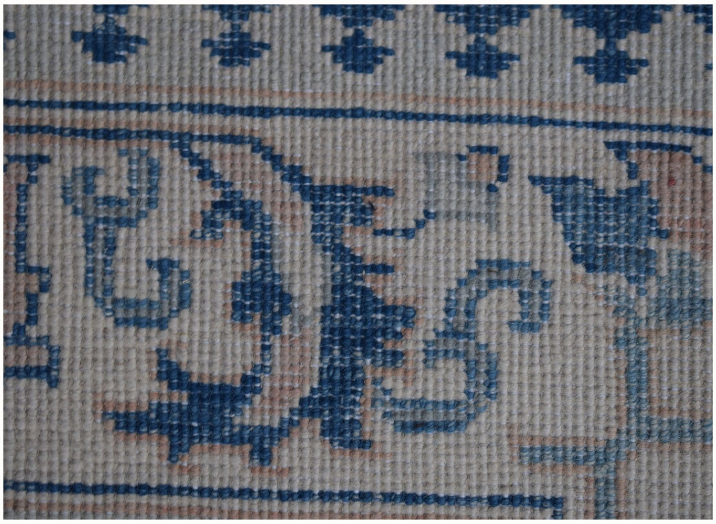A close-up of a handmade Afghan Kazakh runner featuring intricate blue floral patterns on beige.