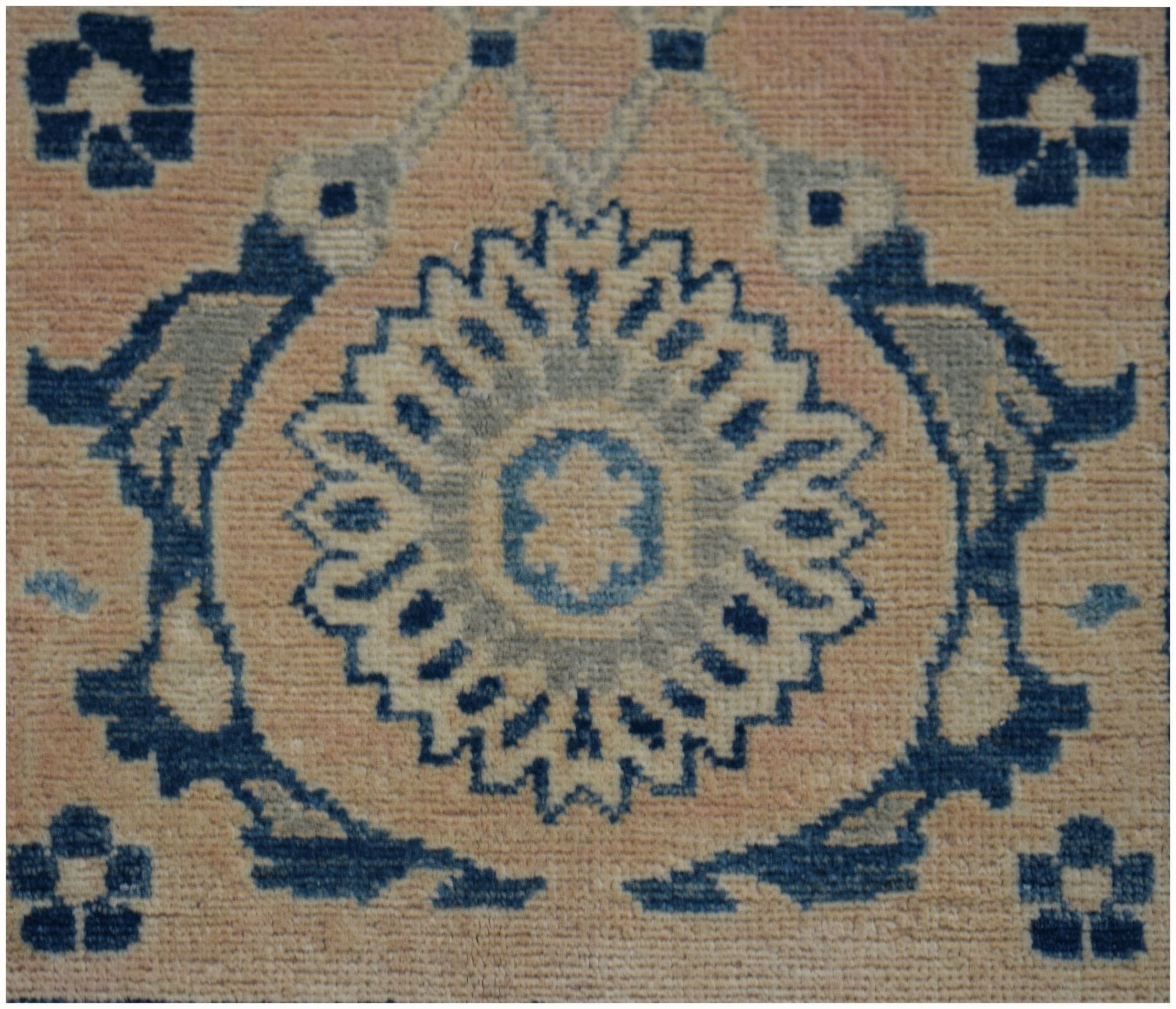 A handmade Afghan Kazakh runner featuring a central blue floral medallion on a beige wool field.