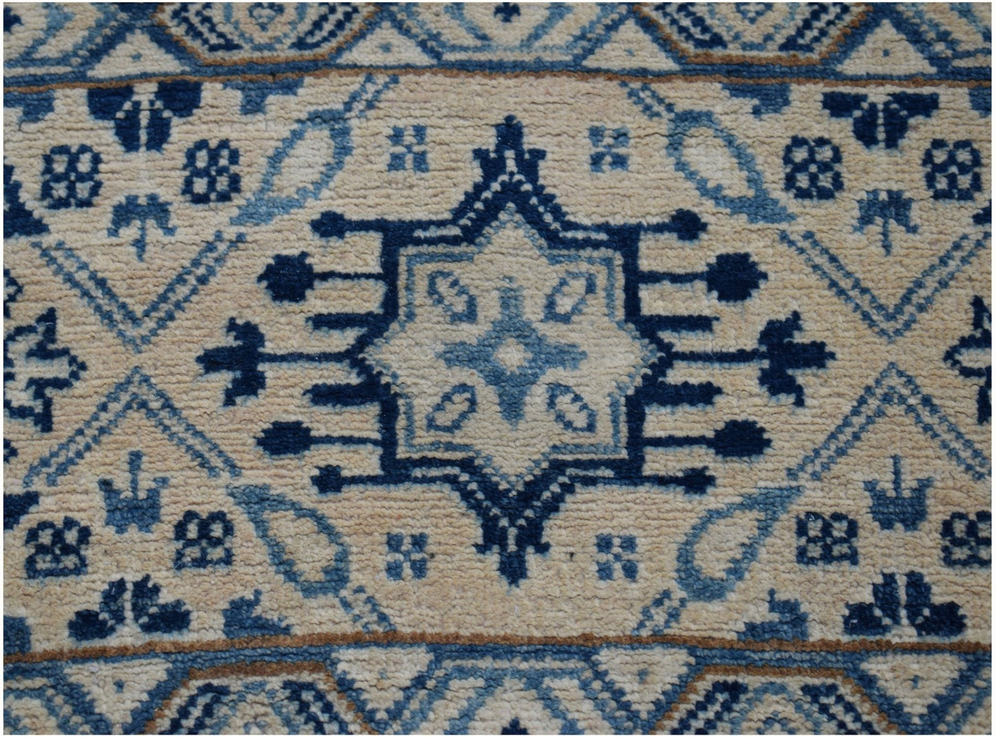 Handmade Afghan Kazakh runner rug featuring a central blue geometric medallion on a beige field.
