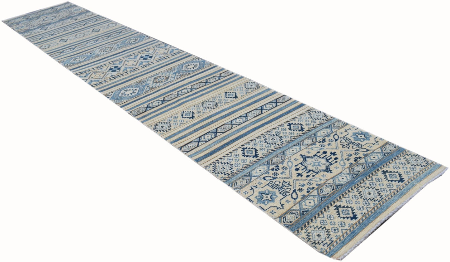 A long, handmade Afghan Kazakh runner rug featuring geometric patterns in blue, beige, and grey.
