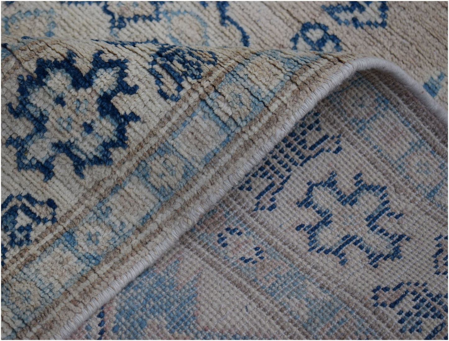 A handmade Afghan Kazakh runner featuring a beige wool pile with blue geometric patterns.