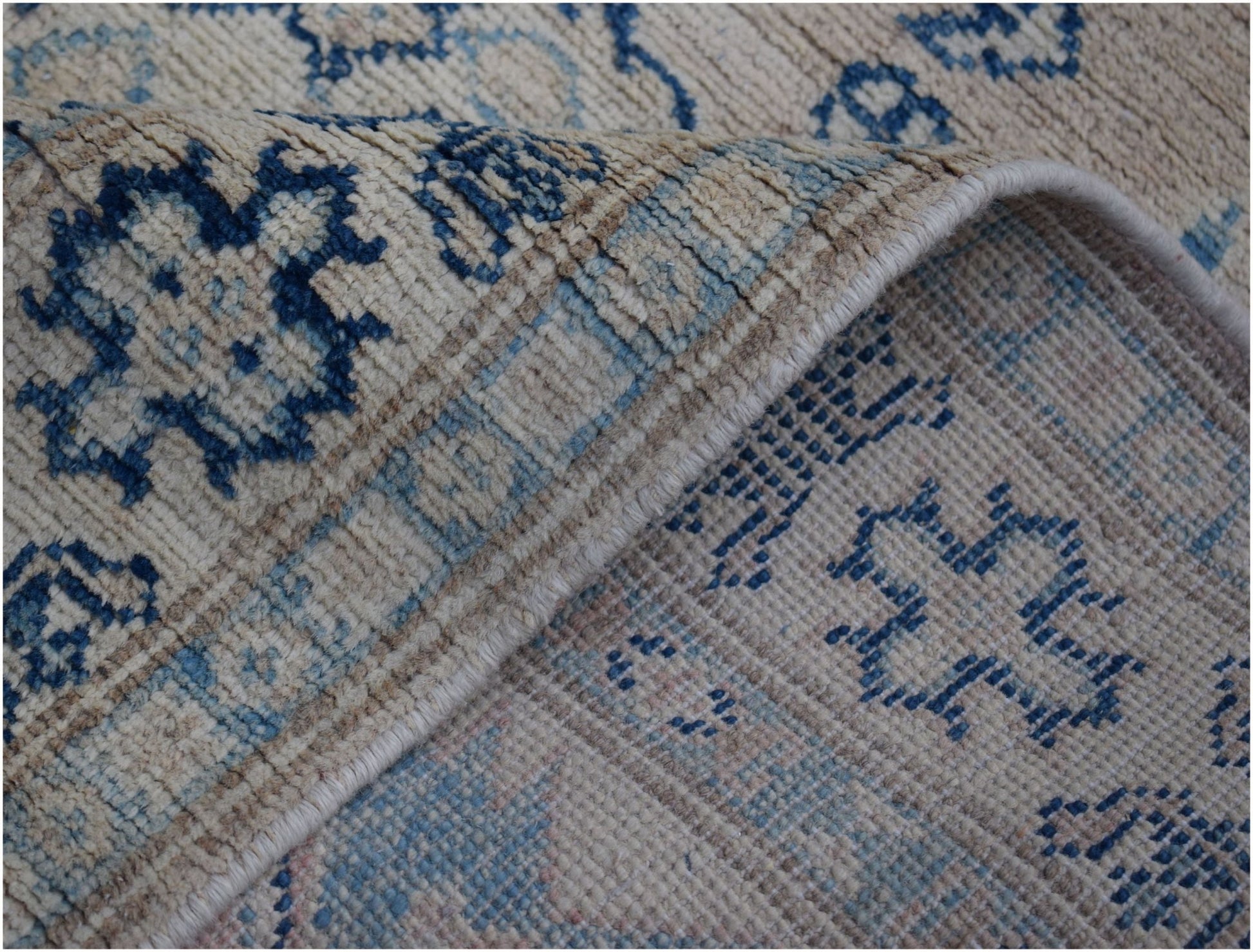 A handmade Afghan Kazakh runner featuring a beige wool pile with blue geometric patterns.