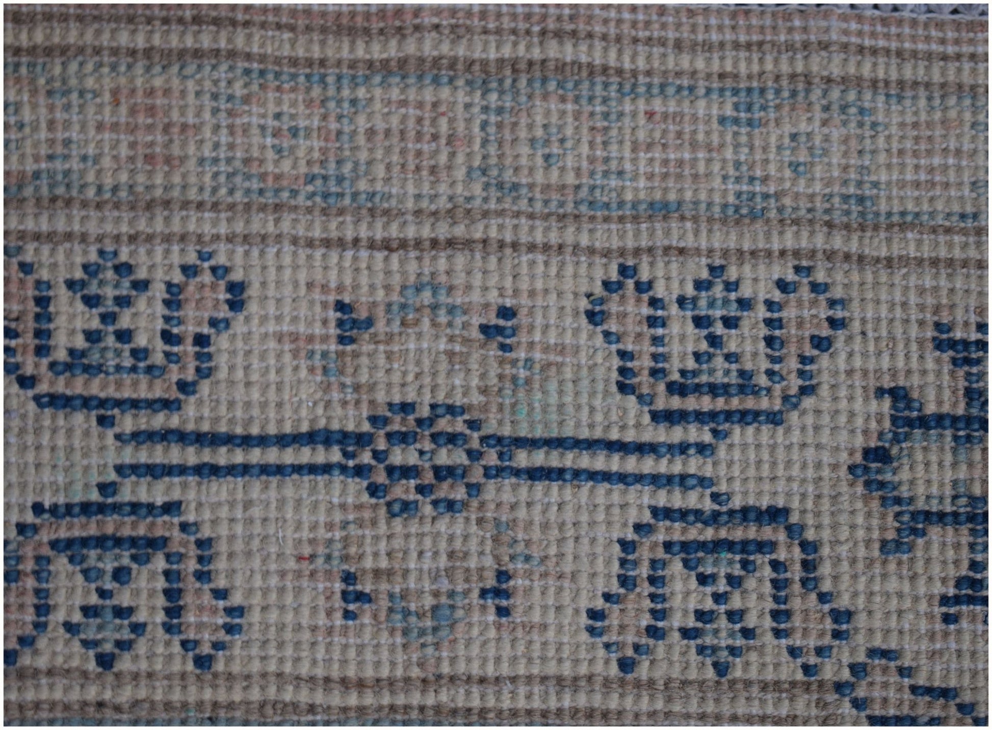 A close-up of an Afghan Kazakh runner rug featuring a beige background with blue geometric motifs.