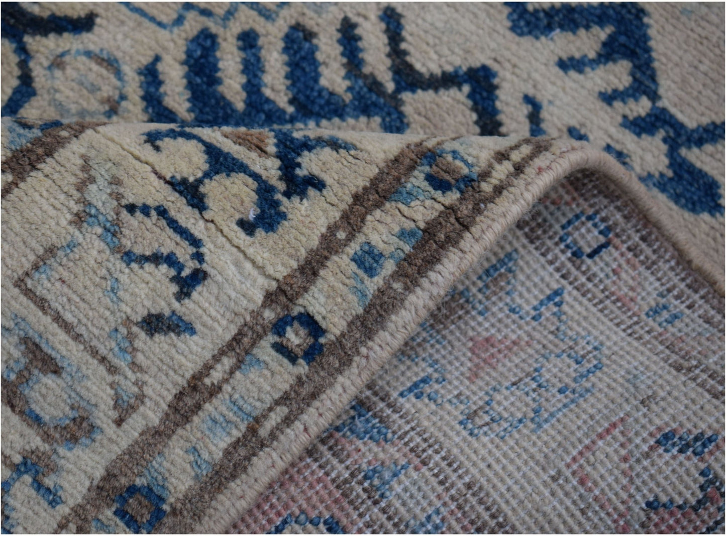 A close-up view of a handmade Afghan Kazakh runner featuring blue and beige geometric patterns.