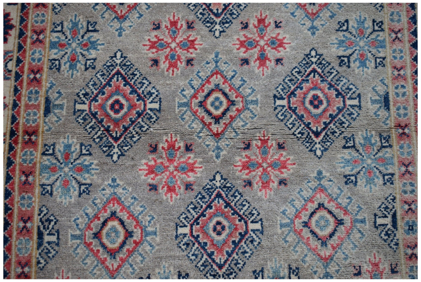 Handmade Afghan Kazakh rug featuring a repeating geometric diamond and floral pattern in red and blue.