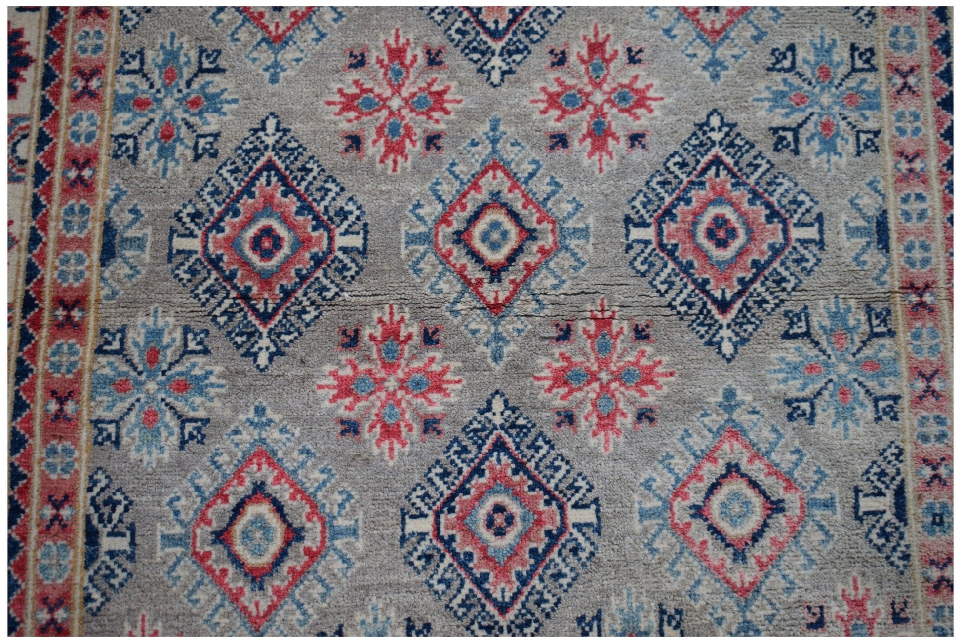 Handmade Afghan Kazakh rug featuring a repeating geometric diamond and floral pattern in red and blue.